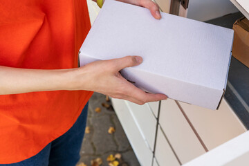 Wall Mural - Person holding a cardboard box. A woman with a box in her hands near the self-service mail terminal. Parcel delivery machine. Mail delivery and post service, online shopping, e commerce concept	