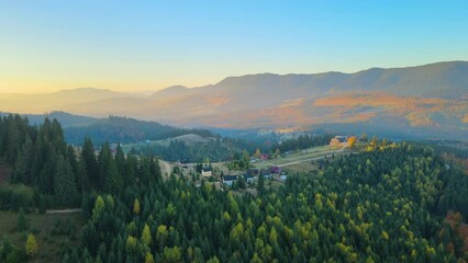 Wall Mural - Wooded hills of Carpathian mountains in Ukraine with small traditional village houses at sunset. Brightly illuminated with setting sun evergreen woods with scattered local homes at fall season