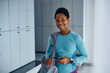 © Drazen - Happy black sportswoman with sports bag and mobile phone at gym's dressing room looking at camera.