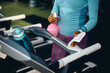 © Drazen - Close up of black athletic woman spraying treadmill with disinfectant before exercising in gym.