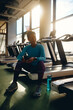 © Drazen - Smiling black athlete using her smart phone while relaxing in gym.