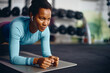 © Drazen - Black athletic woman doing plank exercise while working out in gym.