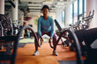 © Drazen - African American athletic woman exercising with battle ropes in gym.