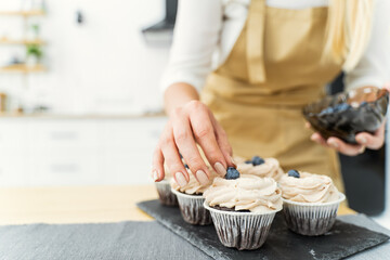 Women's hands of a confectioner, decorating cupcakes
with blueberries and chocolate. Close-up, space for text