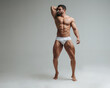 © Serge Lee - Sexy muscular man in white underwear posing in studio. Handsome bodybuilder standing on grey background. Big male model showing his muscles.