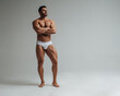 Sexy muscular man in white underwear posing in studio. Handsome bodybuilder standing on grey background. Big male model showing his muscles.