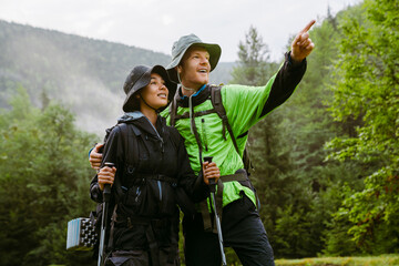 Smiling multiethnic tourist couple pointing and looking aside during hiking