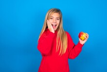 Positive Glad Caucasian Teen Girl Wearing Red Sweater Over Blue Studio Background Says: Wow How Exciting It Is, Indicates Something.  One Hand On His Head And Pointing With Other Hand.