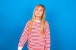 © Jihan - Gloomy, bored caucasian teen girl wearing striped shirt over blue studio background frowns face looking up, being upset with so much talking hands down, feels tired and wants to leave.