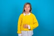 © Jihan - caucasian teen girl wearing yellow sweater over blue studio background touches tummy, smiles gently, eating and satisfaction concept.