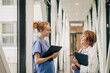 © Maskot - Side view of female healthcare workers discussing while standing in corridor