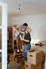 Man Standing On Stool Kissing Boyfriend At Home
