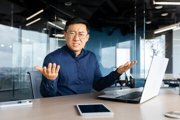 Wall Mural - Portrait of frustrated and angry boss inside office, asian man looking at camera and shouting upset, man at workplace using laptop unhappy with work result.