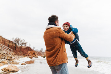 Wall Mural - Father holding son in his arms while spending fun time together on beach