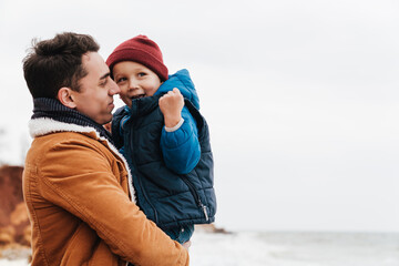 Wall Mural - Smiling father holding son in his arms while spending fun time together on beach