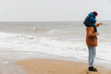 Wall Mural - Son sitting on his father's neck during walk on beach