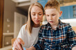 © Drobot Dean - Smiling mom and her son reading book while sitting in cozy kitchen