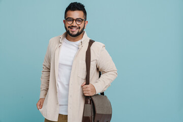 Wall Mural - Indian guy smiling while standing with bag isolated over blue wall