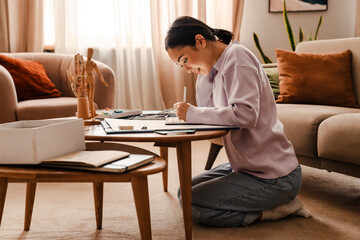 Asian woman drawing on digital tablet with stylus while sitting at table