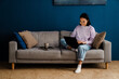© Drobot Dean - Cheerful asian woman working on laptop while sitting on couch