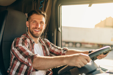 Professional middle aged truck driver in casual clothes driving truck vehicle going for a long transportation route.