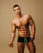 Handsome guy in swimwear posing in studio. Sexy man with six pack abs standing on neutral background. Shirtless male model in underwear.