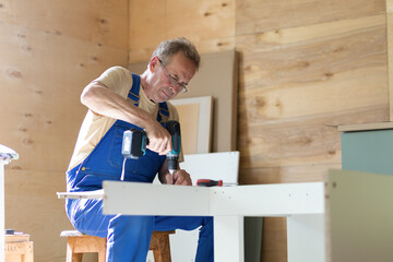 mature adult elderly senior man building wooden house, assembling furniture according to the instruction using different tool, drill, screwdriver. active old age, male hobby retirement