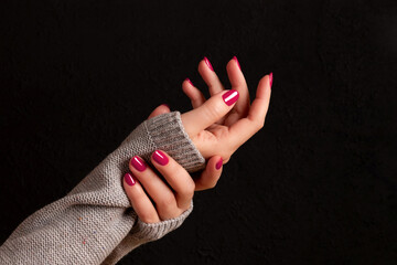 Wall Mural - Female hands in gray knitted sweater with beautiful manicure - viva magenta, pink nails on dark black background. Nail care concept