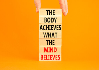 Mind and body symbol. Concept words The body achieves what the mind believes on wooden blocks. Beautiful orange background. Copy space. Businessman hand. Motivational mind and body concept.