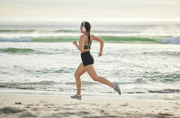 Woman running on beach, listening to music and morning cardio routine for healthy lifestyle in California. Fitness workout by sea, young athlete with headphones and sports exercise in summer