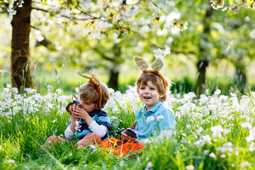 Two little boy friends in Easter bunny ears eating chocolate cakes and muffins