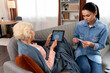 © NFstock - Elderly woman holding tablet and explaining her symptoms to doctor at video call while her daughter measuring her temperature at home. Medicine, technology and healthcare concept