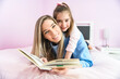 © Louis-Paul Photo - Mom and child daughter are reading a book on bedroom