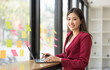 © wichayada - Charming Asian businesswoman sitting in the office with a digital laptop computer. Excited Asian businesswoman raising hands to congratulate while working in a modern office,