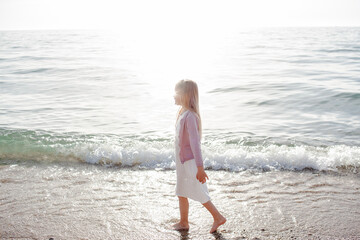 The 6 years blonde girl walking in the beach. The child dress white sundress