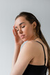© LIGHTFIELD STUDIOS - portrait of brunette woman in black top posing with closed eyes isolated on gray.