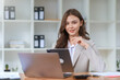 © amnaj - Pretty Asian businesswoman sitting smiling and happy working on laptop computer and document in office. Looking at camera.
