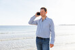 © Enigma - Businessman Talking On Phone, using smartphone mobile apps texting message, surfing social media tech standing on the city beach against the backdrop of the sea