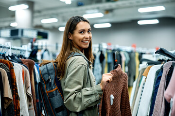 Young happy woman shopping at clothing store and looking at camera.