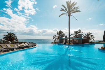 Wall Mural - Beautiful summer exotic ocean view with swimming pool, palm trees, blue sky and sunbeds in Madeira island. Hot summer day