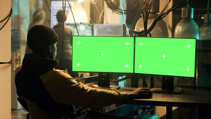 Mysterious criminal using greenscreen display to hack web network, planning phishing attack at night. Man doing illegal activity with isolated chromakey template and mockup, security breach.