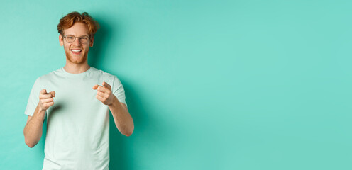 Wall Mural - Handsome young man with ginger hair, wearing glasses and t-shirt, pointing finger at camera and smiling, choosing you, congratulating or praising, standing over mint background