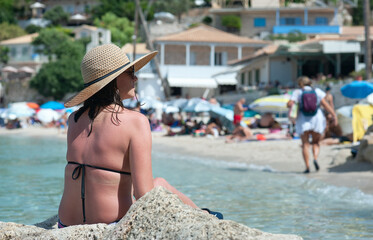 Wall Mural - A young woman is sitting on the rock at Agios Nikitas beach