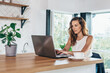 © undrey - Woman is sitting at the kitchen table with laptop