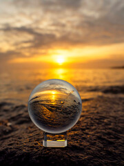 Wall Mural - glass ball on a rough stone by the ocean, sunset sky in the background. warm soft light. selective f