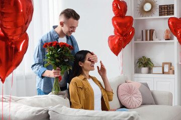 Wall Mural - Boyfriend presenting beautiful bouquet of roses to his girlfriend in room decorated with heart shaped balloons. Valentine's day celebration