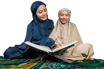 Asian Muslim mother and daughter in a hijab on a prayer rug reading the Quran