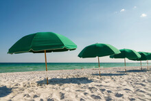 Beach At Destin, Florida With Row Of Green Umbrellas Near The Ocean. There Is A White Sand And Beach Umbrellas Against The Ocean Waves And Blue Sky.