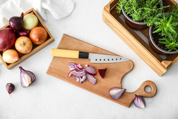 Wall Mural - Composition with wooden board with cut onion, knife and herbs on light background