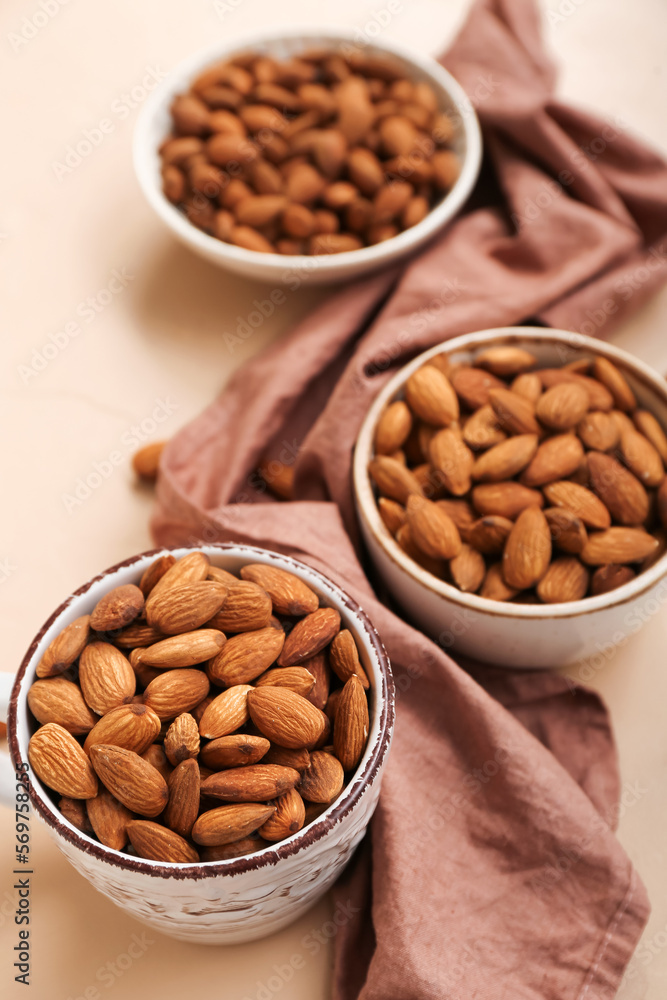 Bowls and cup with almond nuts on color background, closeup
